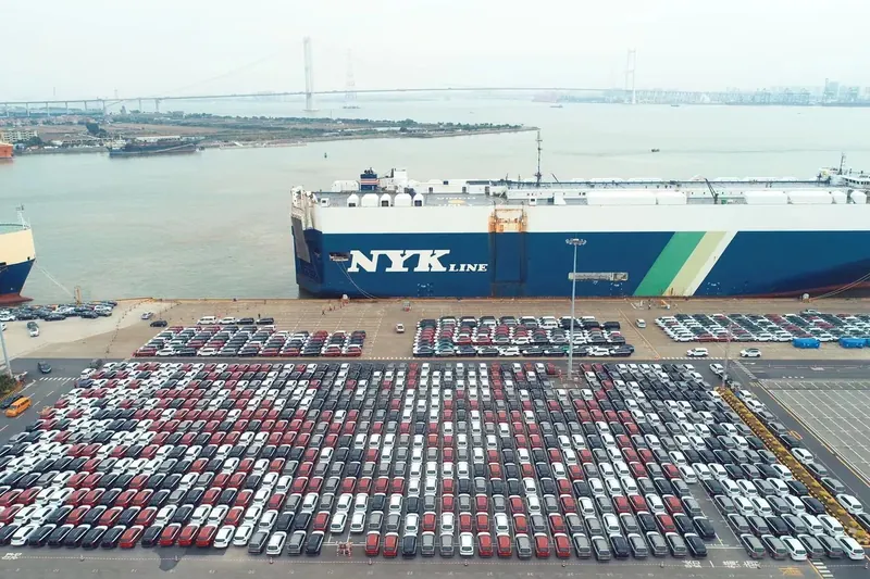 Export vehicles staged at an auto terminal beside a car carrier